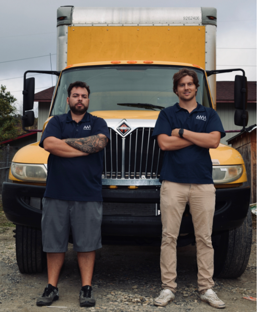 Two uniformed professional movers stand in front of a yellow moving truck, snapshot
