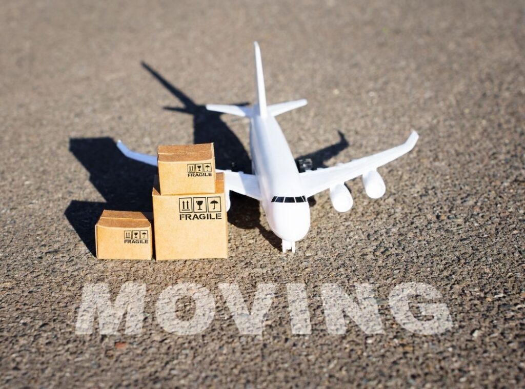 tiny toy-sized airplane and moving boxes placed just behind "MOVING" painted white on asphalt