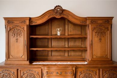 Ornate antique wooden credenza with cabinets and shelves on top, drawers on bottom, against a white wall