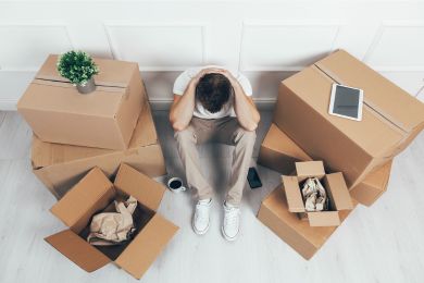 Overhead shot of a man sitting against a wall between moving boxes, head in hands, looking defeated.